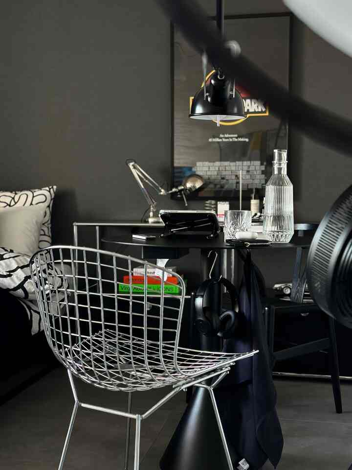 Modern home office in black and silver tones featuring metal chair, desk, and framed poster on dark wall with minimal design
