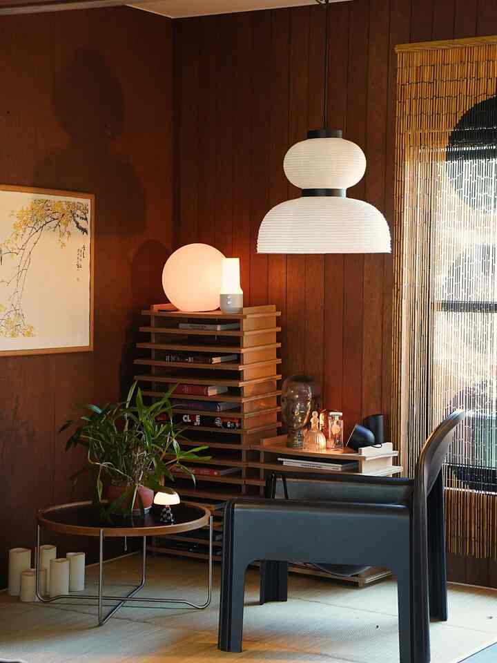 ブラウン調の小さなリビング、黒いラウンジチェアと丸いコーヒーテーブル、木製の棚と照明が調和した雰囲気のあるインテリア