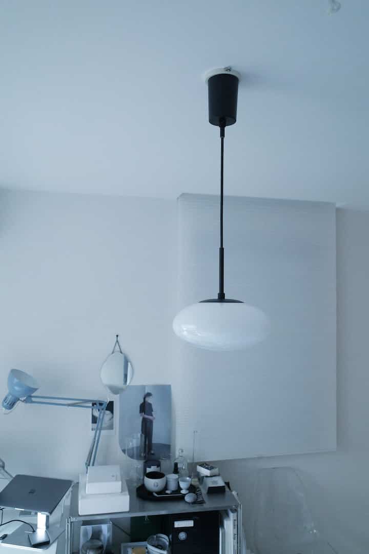 モノトーンとホワイトを基調としたホームオフィス空間、白い楕円形のペンダントライトと青い作業用ライトが配置されたミニマルな部屋