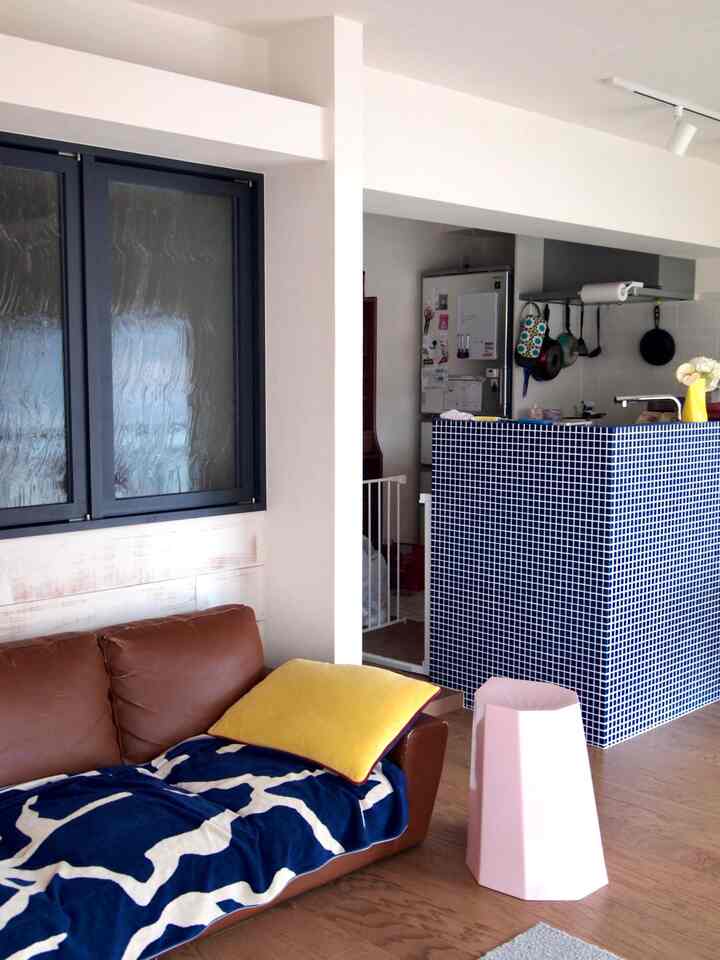 Blue and yellow accented living room and kitchen space featuring a brown sofa and a pink stool with a warm atmosphere