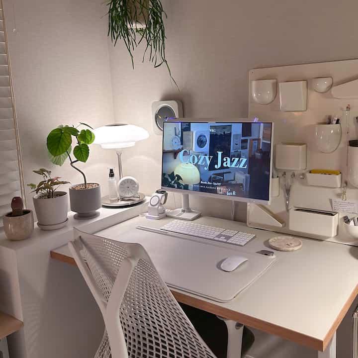 White and beige toned home office featuring desk, monitor, plants, and lighting in a tidy setup
