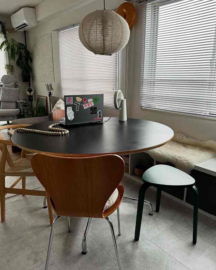 Simple living room with a black round dining table, wood-toned chairs, and a cat cushion near the window for a single occupant