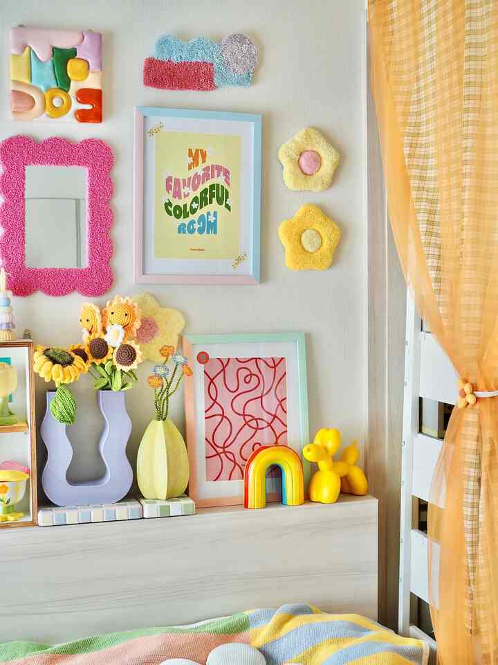 ベージュの壁と黄色の装飾がある子供部屋、フレームポスターや花瓶、オレンジ色のカーテンが配置された明るくかわいらしい空間
