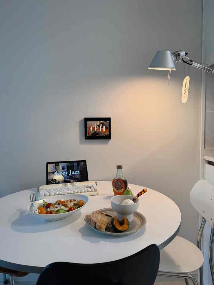 白とシルバーの色調のキッチンダイニングスペース、丸テーブルに料理と柔らかな照明が配置されたシンプルな雰囲気のインテリア