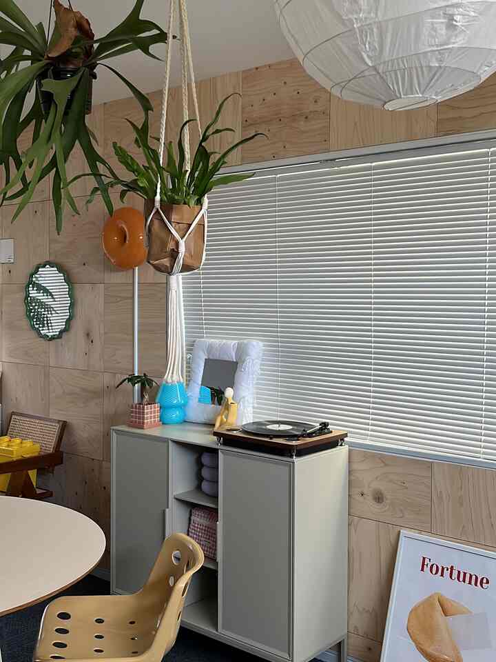 ホワイトのブラインドと木目調の壁が調和した狭い部屋、レトロなレコードプレーヤーとダイニングチェアが配置された雰囲気あるインテリア