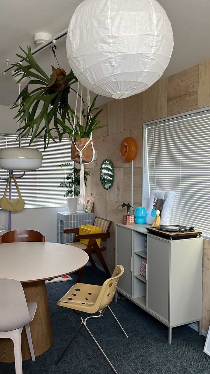 木目調の壁とライトブラウンのダイニングテーブル、白い照明と植物が配置されたミッドセンチュリーモダンのダイニングルーム