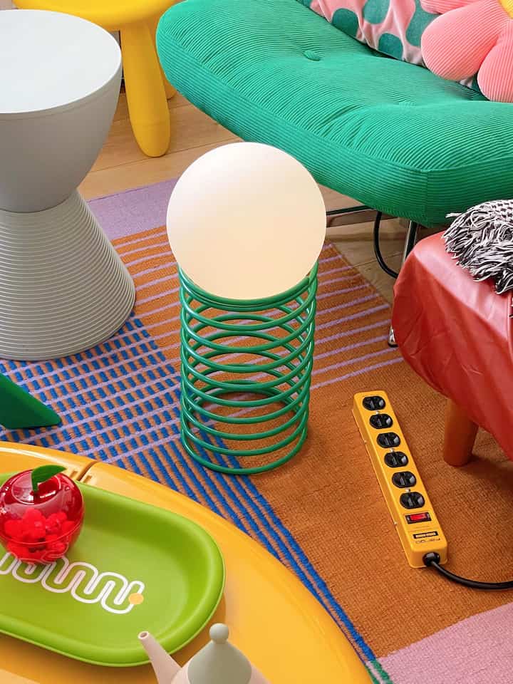 明るくカラフルな色調のリビング、スプリング形状のフラワースタンドに球形のボールランプが配置されたレトロなインテリア