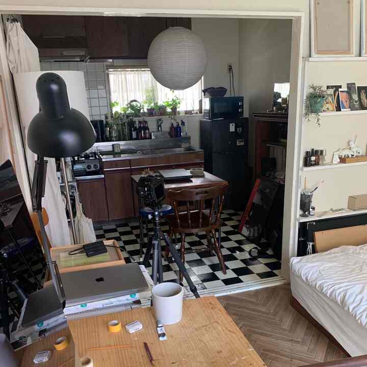 A white and black toned studio apartment featuring a desk, bed, and kitchen in one simple home office space