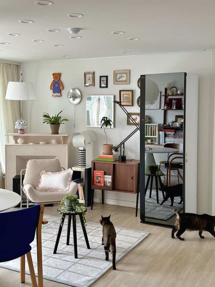 Bright natural modern living room featuring a large black-tinted full-length mirror, vintage wood console, and two cats creating a cozy atmosphere