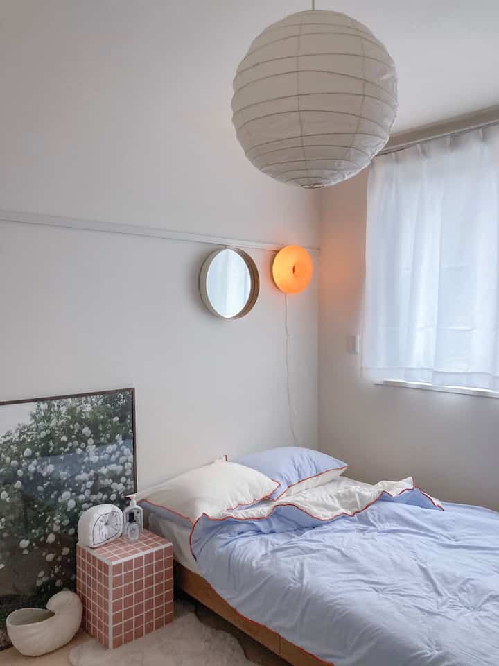 白と青の色調の寝室、ミッドセンチュリーモダンスタイルのタイル製ナイトテーブルと丸い壁掛け照明が配置された落ち着いた空間