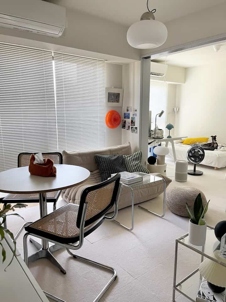 ベージュとホワイトのトーンの2Kアパートのリビングと寝室、ソファとダイニングテーブルが配置されたモダンで清潔感のある空間、ベッドに犬がいる