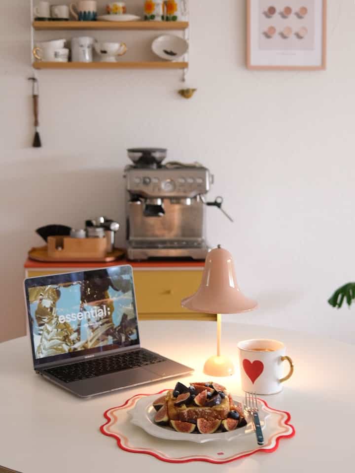 White-toned small kitchen corner featuring a round dining table, coffee machine, and table lamp creating a cozy home cafe vibe