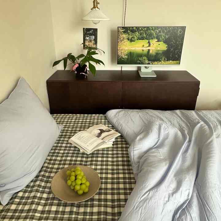 White and dark brown toned bedroom featuring a check-patterned mattress and a monitor on a sideboard, creating a cozy atmosphere