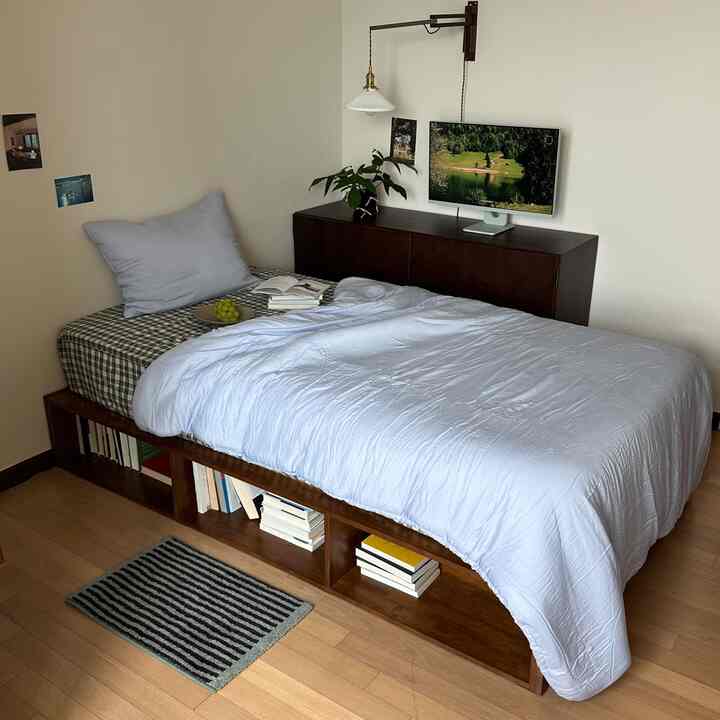 Cozy bedroom in soft pastel blue and checkered bedding featuring a wooden sideboard, wall sconce, and small striped rug