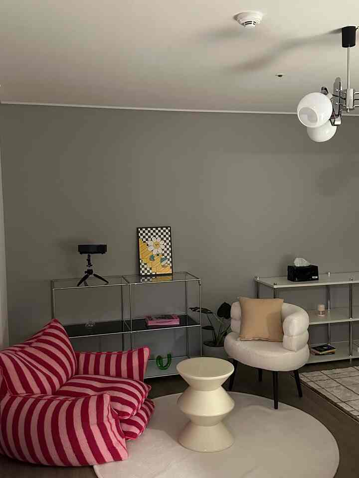 グレーの壁とホワイトのラグの上に、ピンクのストライプのビーンバッグとベージュクッションのアームチェアが配置された書斎兼リビングルーム