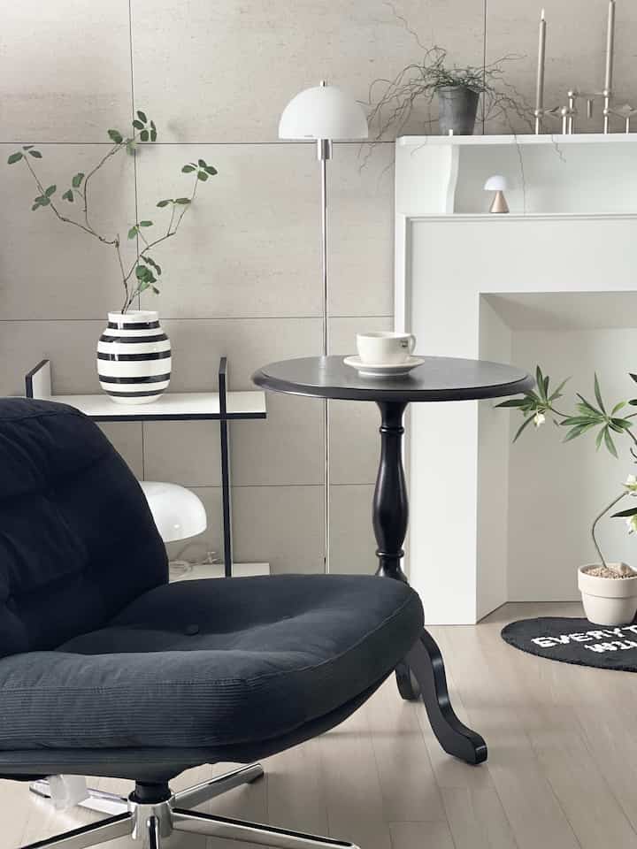 A white and black toned living room featuring a black armchair and a side table with a coffee cup in a clean modern interior