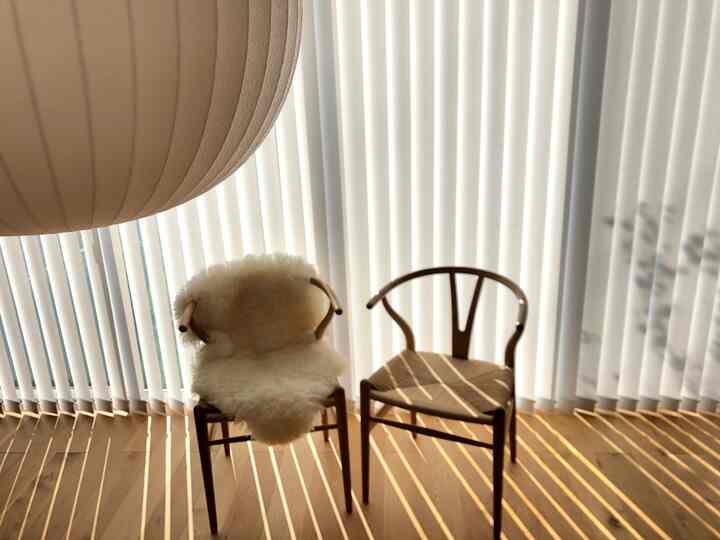 暖かい木目調のナチュラルモダンなバルコニー空間に、Yチェアとシープスキンカバー、ペンダントライト、バーチカルブラインドが配置された落ち着いた雰囲気のインテリア