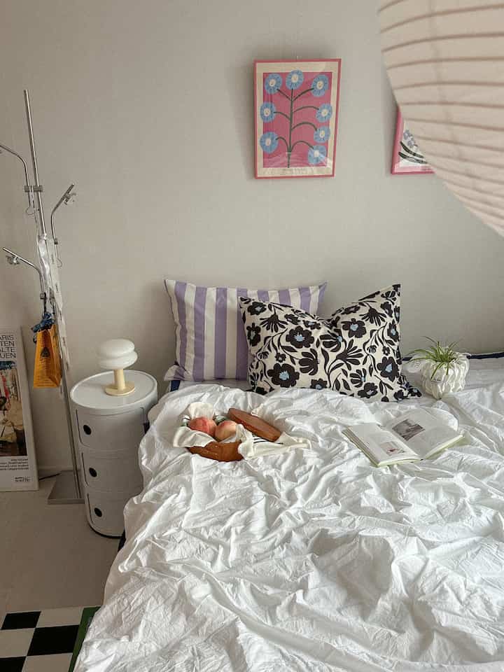 White and natural tone bedroom featuring a tidy bed with cushions, nightstand, and wall decor creating a cozy space