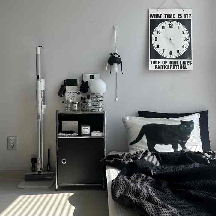 黒と白のトーンの寝室、モダンな雰囲気でナイトテーブルと照明、猫の柄の枕が配置された空間