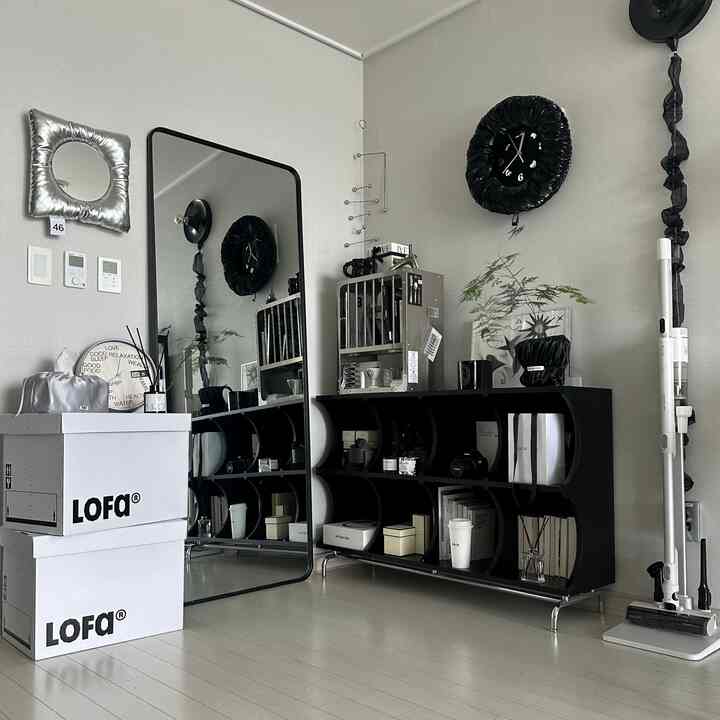 Minimal entrance space in black and white tones featuring a large full-length mirror, black storage rack, and a wall clock