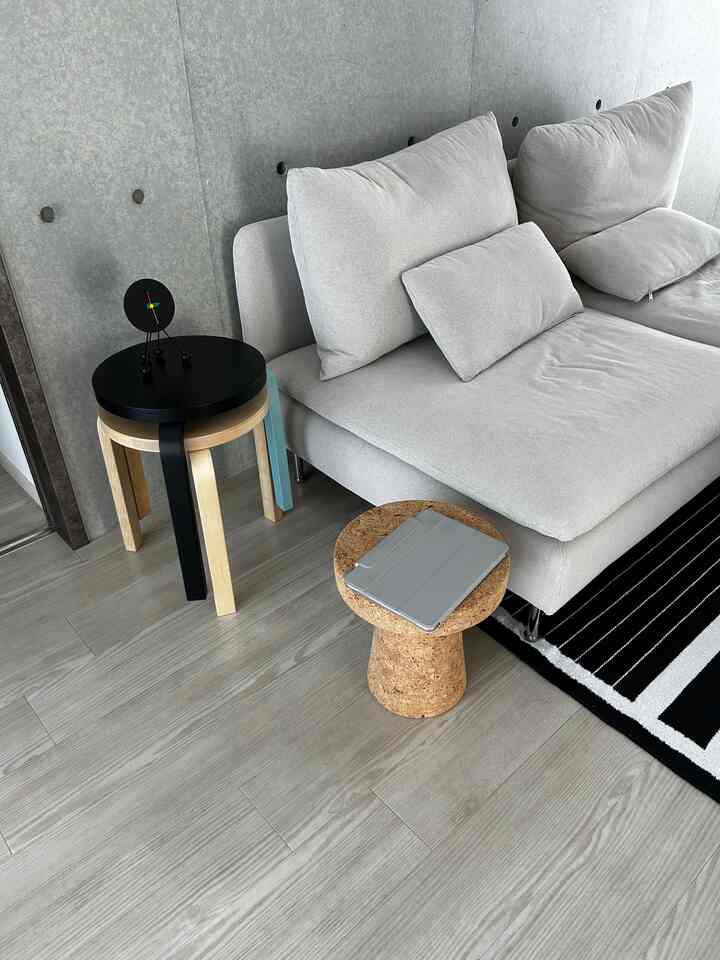 グレーのソファ、コルクスツール、黒い天板の木製スツールが配置されたナチュラルでモダンなリビングルーム