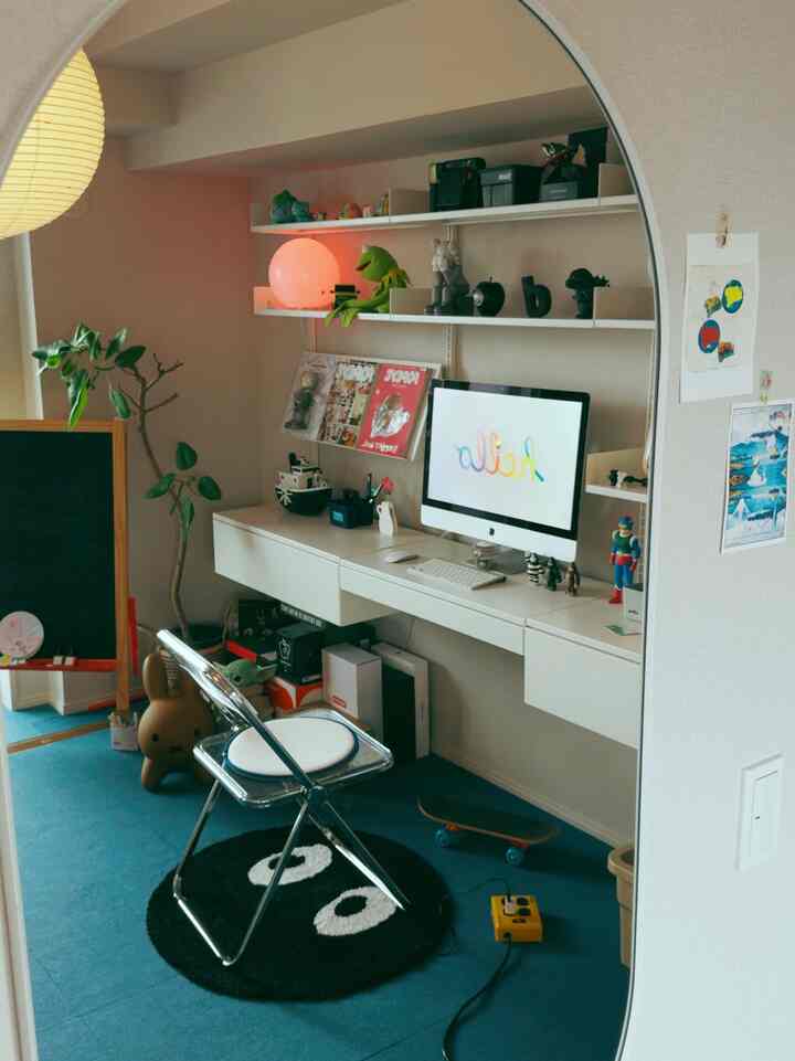Blue floored compact workspace featuring white desk, chrome chair, and computer with playful decor