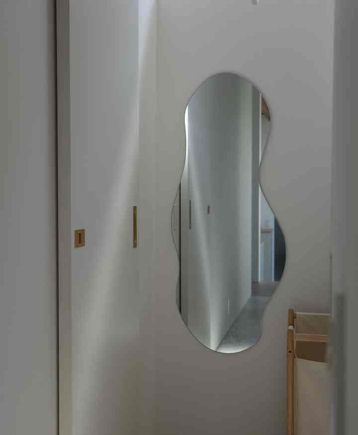 Natural-toned compact dressing room featuring an irregular wall-mounted mirror and gold door handles in a minimal setting