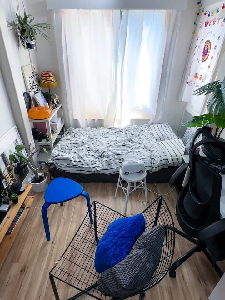 Bright wooden floor and white curtains in a compact studio bedroom, featuring a blue stool and green plants in a natural setting