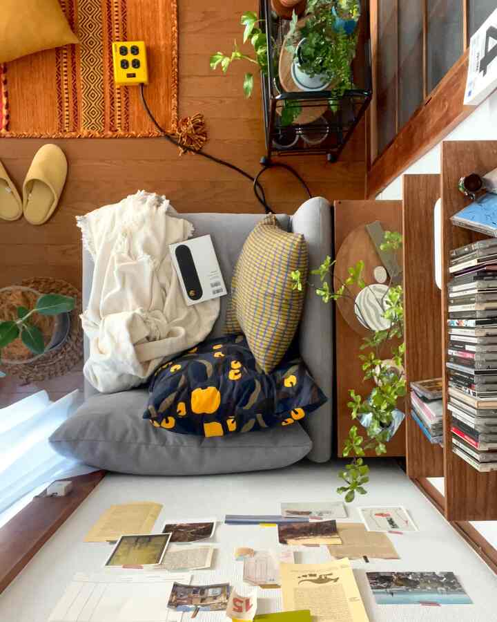 白とオレンジのトーンのリビング、グレーのソファとオレンジのラグ、植物や本棚が配置された雰囲気のあるインテリア