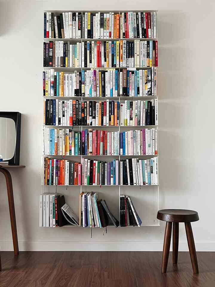 White and wood-toned bedroom study featuring tidy bookshelf and round wooden stool creating cozy ambiance