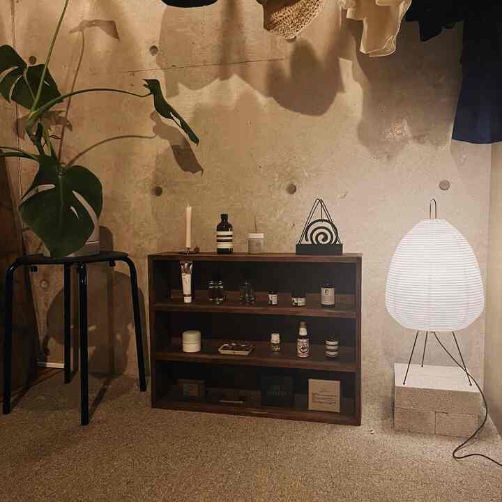 ナチュラルな色調の小さな部屋、コンクリート壁、木製の棚、フロアランプと植物が配置された雰囲気のあるインテリア