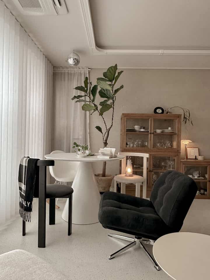 Natural modern tone living room featuring a white round dining table, wood-tone cabinets, and black cushioned chairs creating a cozy space