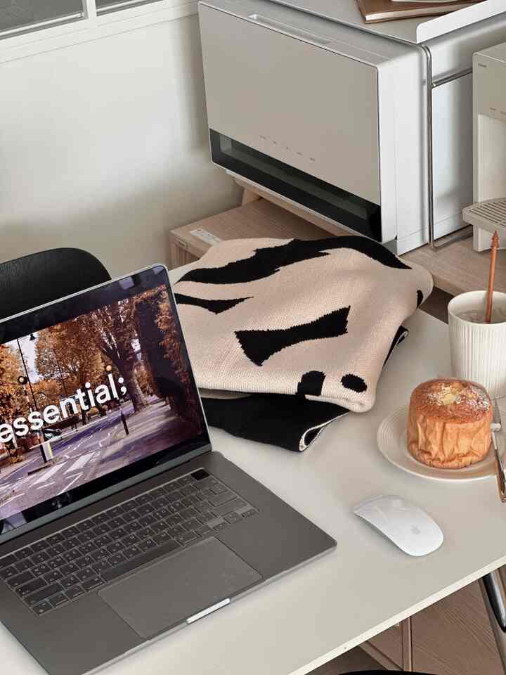 Modern home office with white tone featuring Apple MacBook, Magic Mouse, and a light snack on the desk