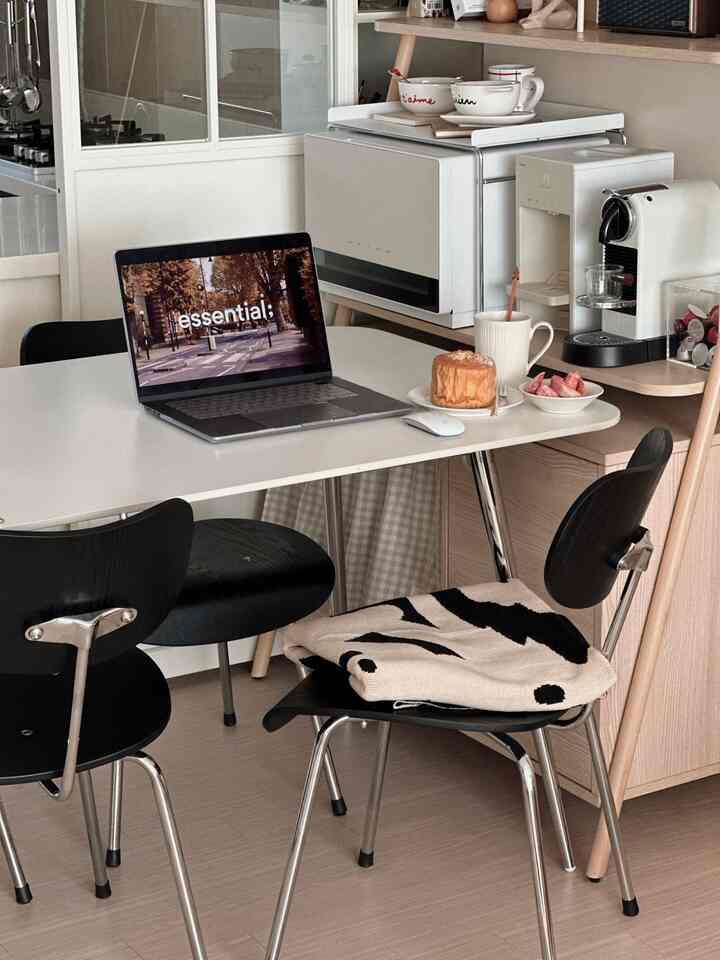 ホワイトとブラックの調和があるコンパクトなキッチン兼おうちカフェ空間、ダイニングテーブルとチェア、コーヒーマシンとノートパソコンが配置された雰囲気のあるインテリア