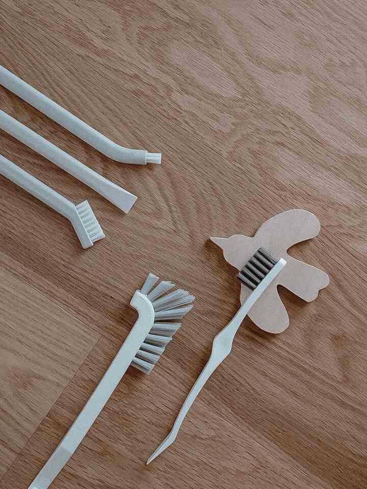 White cleaning brushes of different shapes arranged on brown wood tone background in a simple composition