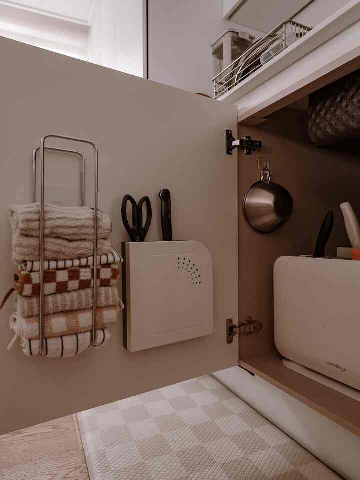 ホワイトとベージュの色調のキッチン収納内、タオル掛けと調理道具が整然と配置された印象的な空間