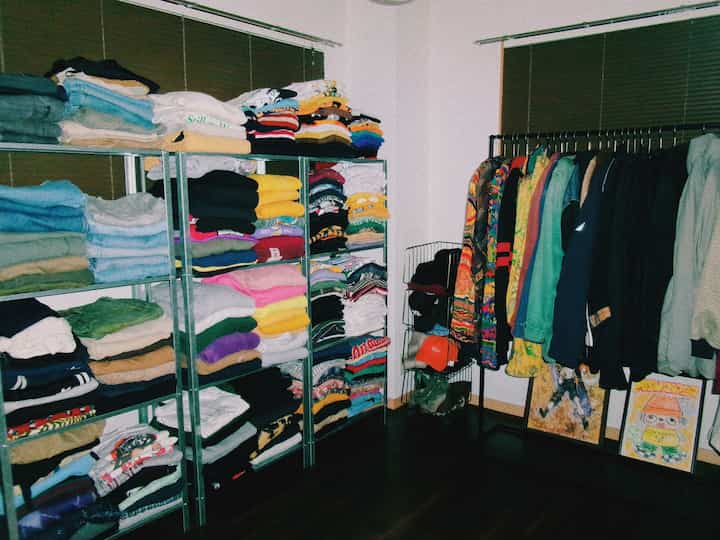 ナチュラルカラーの2DKウォークインクローゼット、白い壁と茶色の床に、メタルシェルフとハンガーラックが並び、多彩な衣類が整然と収納された印象的な空間