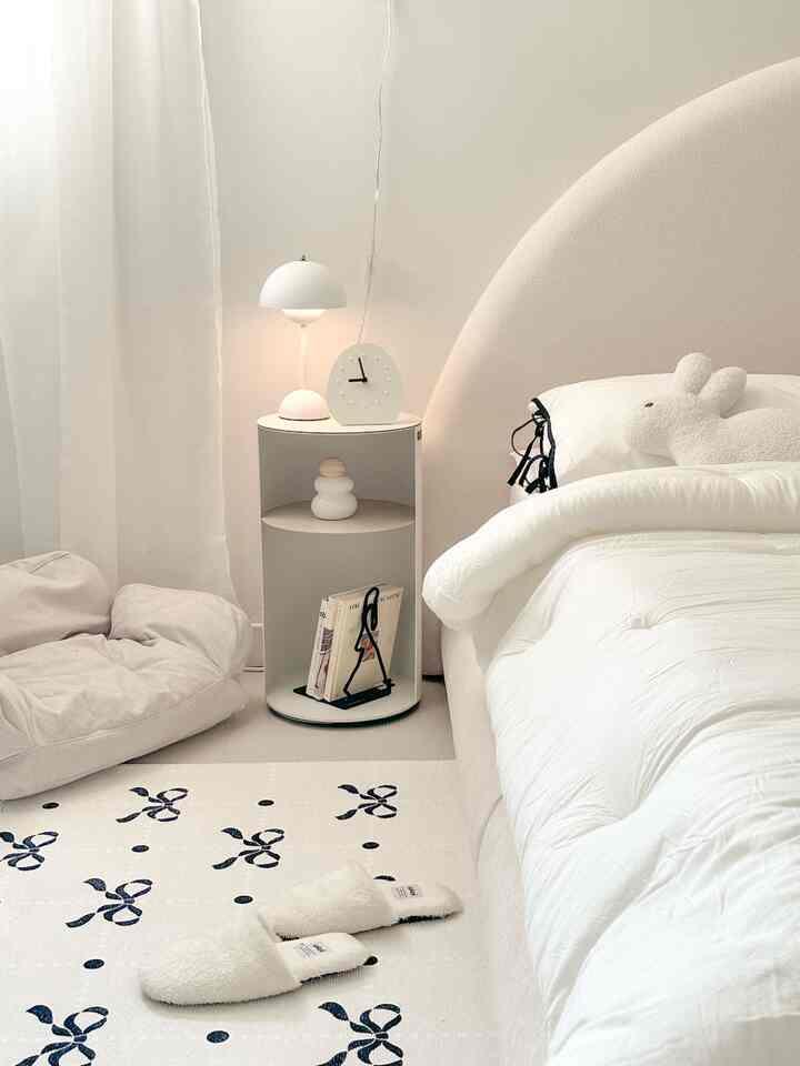 柔らかなナチュラルカラーの寝室、曲線のヘッドボードベッドとナイトテーブルのテーブルランプが配置されたシンプルで居心地の良いインテリア