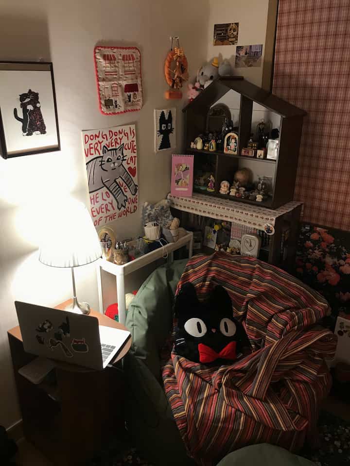 自然な色調の小さな部屋にビーズクッションと猫の形のクッション、テーブルランプ、ヴィンテージスタイルの小物が配置された雰囲気のあるインテリア