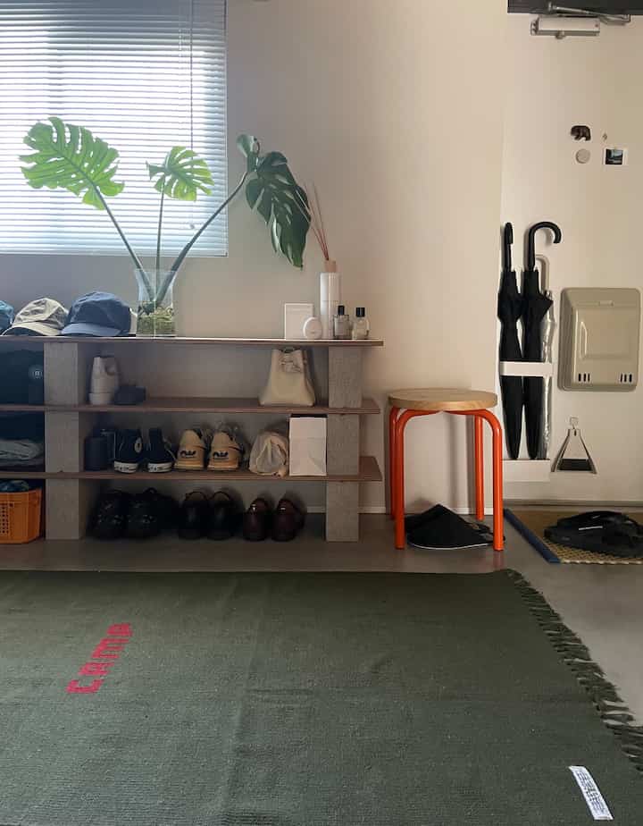 モノトーンを基調としオレンジのアクセントが映える玄関、コンクリートブロックの棚とオレンジスツールが配置されたすっきりとしたインテリア