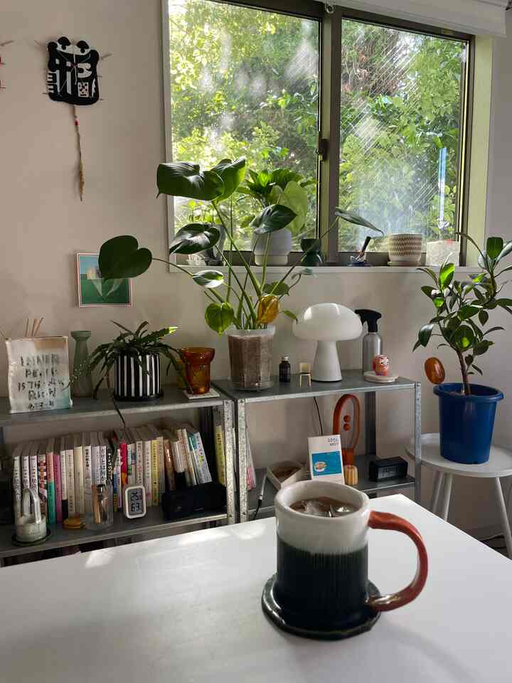 Natural light-filled single household home office featuring desk, shelves, and abundant green plants creating a cozy atmosphere