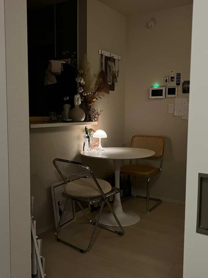 White-toned compact dining area beside kitchen featuring a round table and two chairs, with simple ambiance