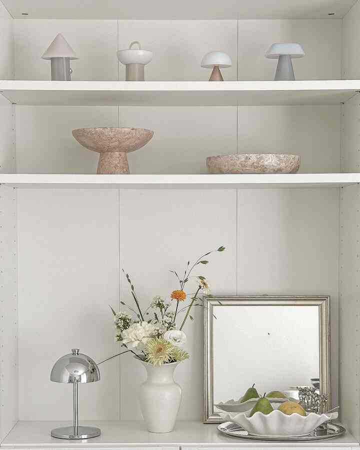 白とシルバーの棚にヴィンテージのオブジェと花飾りが配置された、モダンな雰囲気のインテリア小物のディスプレイ