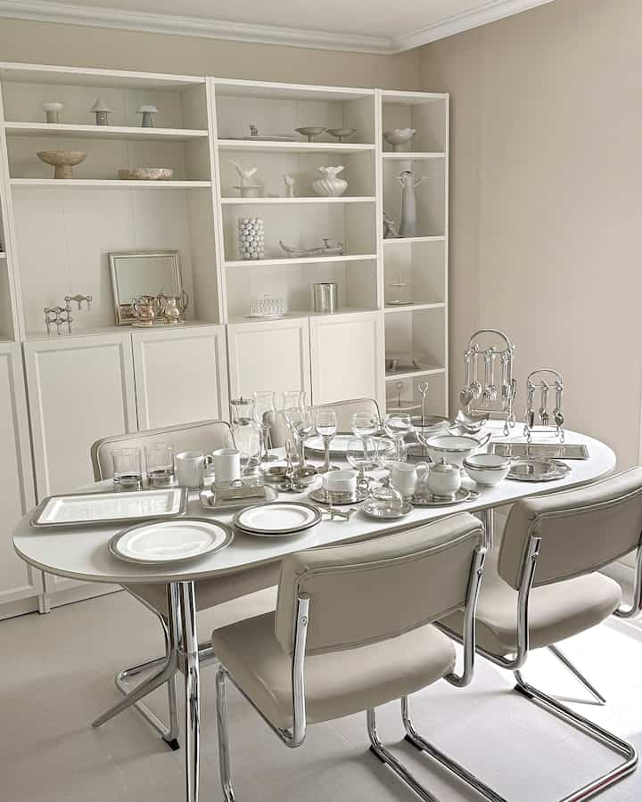 白とベージュのトーンのダイニングルーム、ホワイトの本棚とセラミックの食器が配置されたモダンで清潔感のあるインテリア