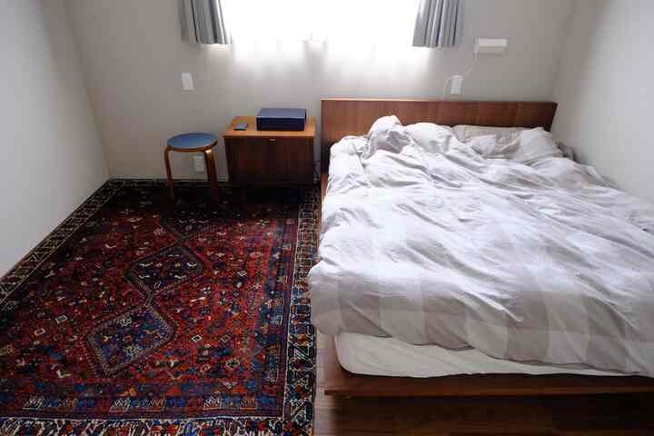 Small bedroom featuring warm wood tones and gray bedding with a bed, stool, and nightstand arranged simply