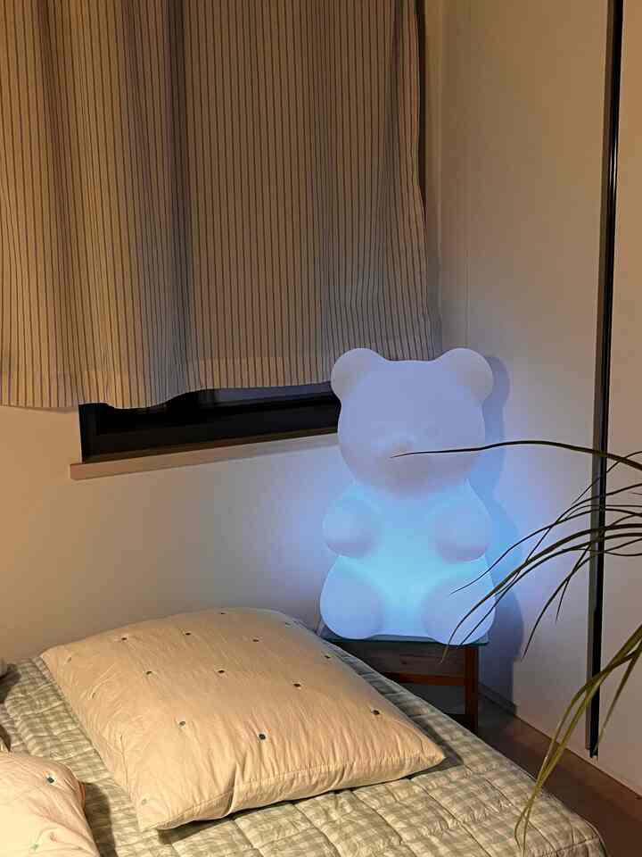 ベージュとグレーのトーンのワンルーム寝室、ベッドとクマ型の間接照明が配置された雰囲気のあるインテリア