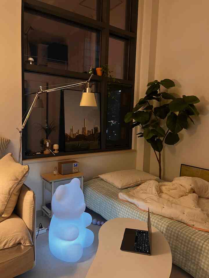 ほのかなベージュ色調のワンルーム寝室、かわいいクマ型ムードランプとフロアランプが配置された雰囲気のあるインテリア