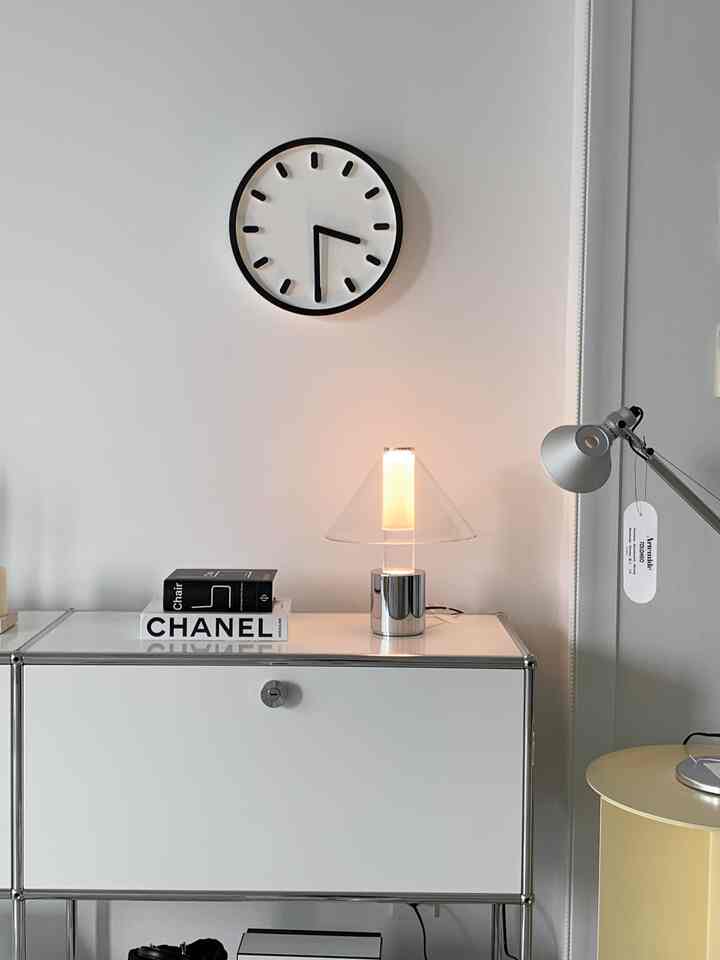 A minimalist modern entrance space in white and gray tones featuring a wall clock, table lamp, and a sleek storage cabinet with clean layout
