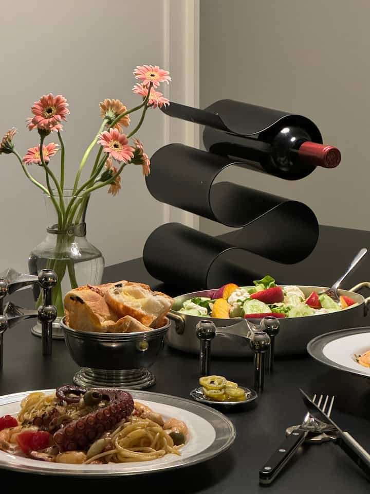 Black-toned dining table space featuring a wine rack, vase with flowers, and stylish bowls and plates in a home party atmosphere