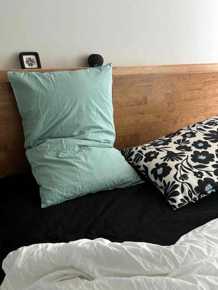 ホワイトとブラックの寝具が置かれた木目調ヘッドボードのシンプルな寝室